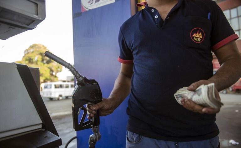 عامل مصري في محطة بنزين يحمل خرطوم تعبئة في يد ونقود في آخر بينما يقف في انتظار لملء العربة التالية ، في العاصمة القاهرة في 29 يونيو 2017. أ ف ب