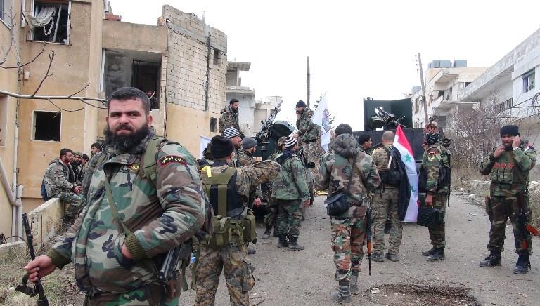 قوات الحكومة السورية تقف في شارع يحمل أعلاماً وطنية. ا ف ب