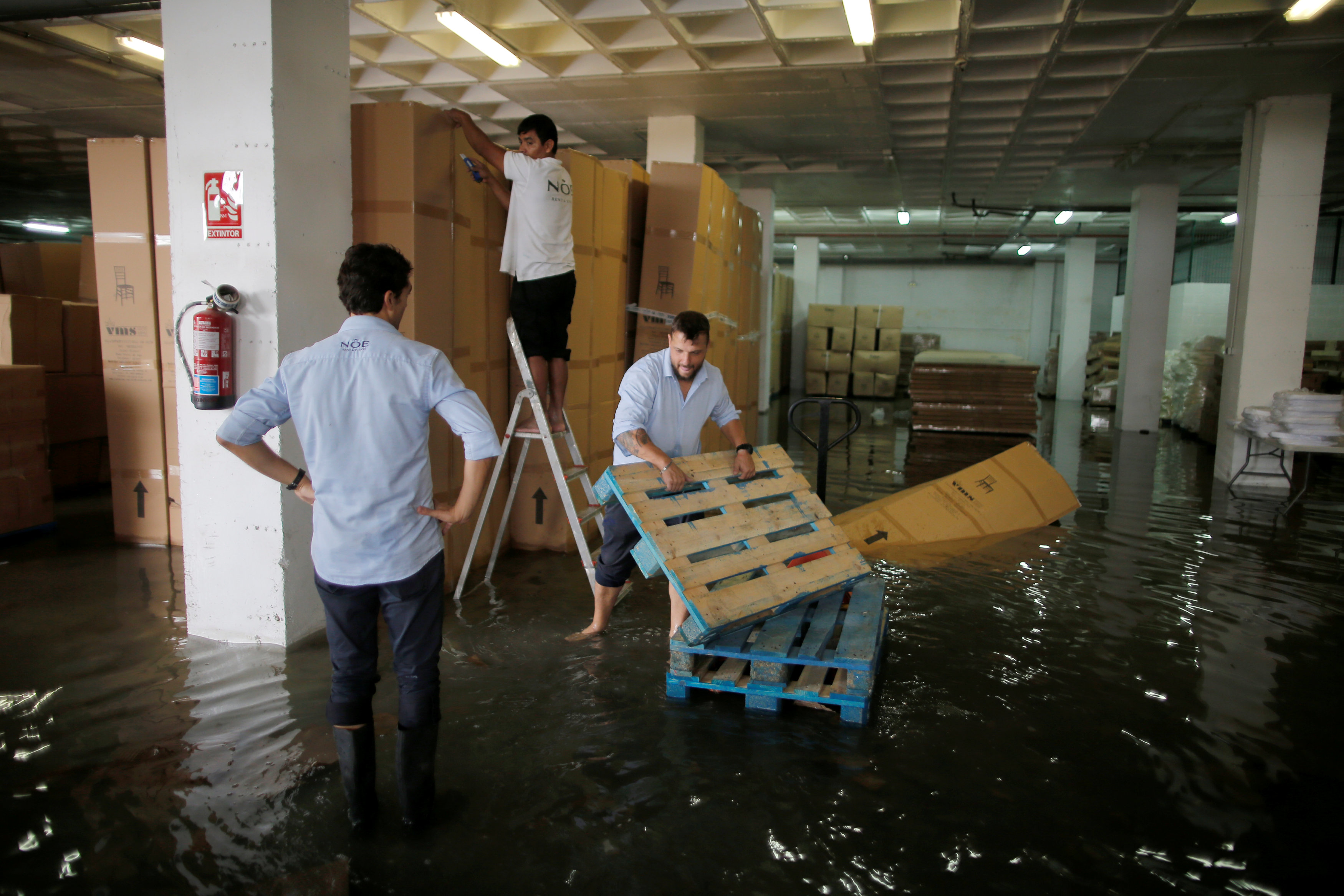 عمال يزيلون الصناديق من مستودع بعد تساقط أمطار غزيرة في جزيرة مايوركا الإسبانية. جون نازكا/ رويترز