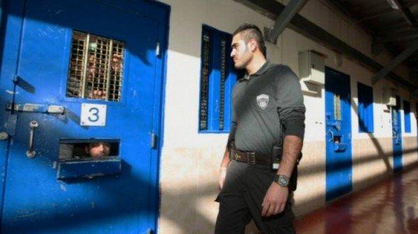 صورة أرشيفية لجندي إسرائيلي يمر أمام إحدى زنزانات الاحتلال التي تضم أسرى فلسطينيين. (وفا) 