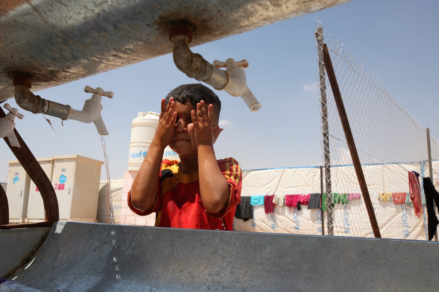 طفل يغسل وجهه من حرّ الشمس في إحدى مخيمات اللاجئين في الأردن. صلاح ملكاوي/ المملكة