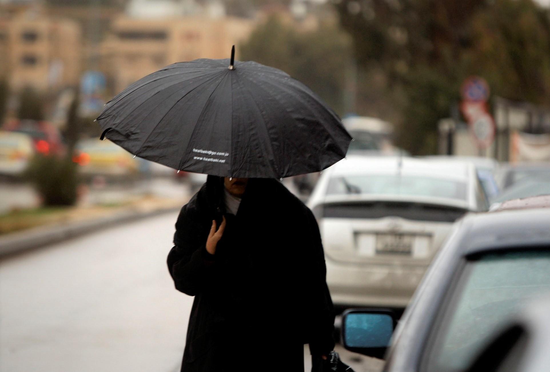 سيدة تحتمي بمظلة من المطر في عمّان. صلاح ملكاوي / المملكة