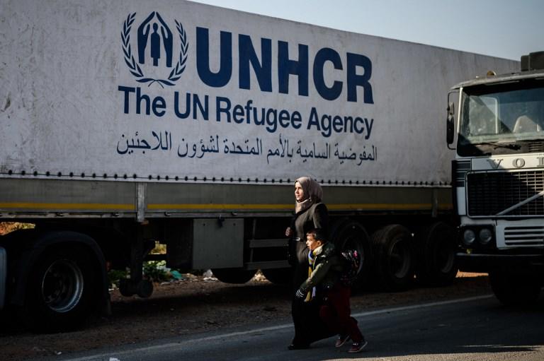 صورة أرشيفية للاجئة مع طفلها يسيران بجانب شاحنة تابعة لمنظمة الأمم المتحدة لشؤون اللاجئين. (أ ف ب)