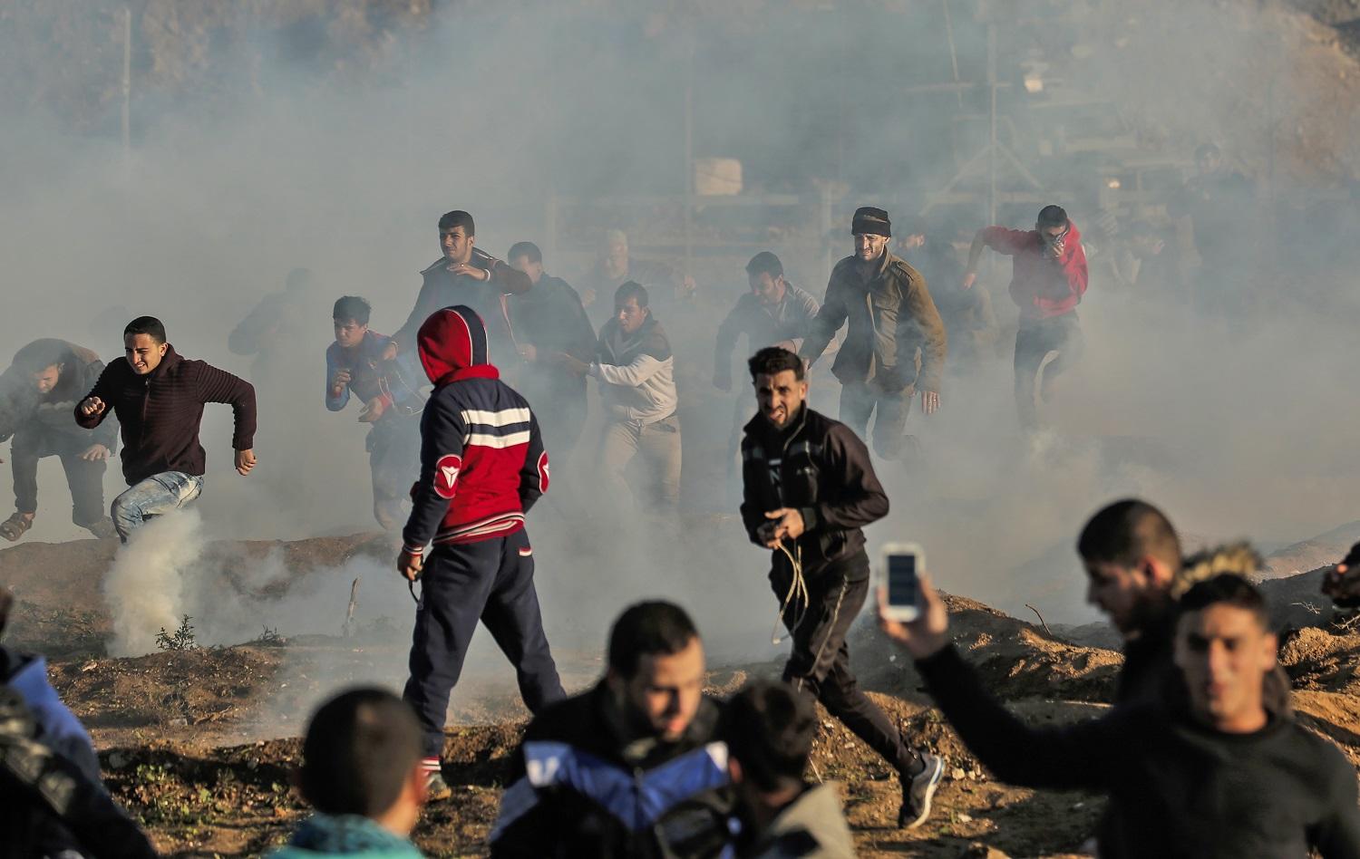 فلسطينيون مشاركون في مسيرات العودة يركضون مبتعدين عن قنابل غاز مسيل للدموع أطلقتها قوات الجيش الإسرائيلي، 11 يناير 2019. أ ف ب  