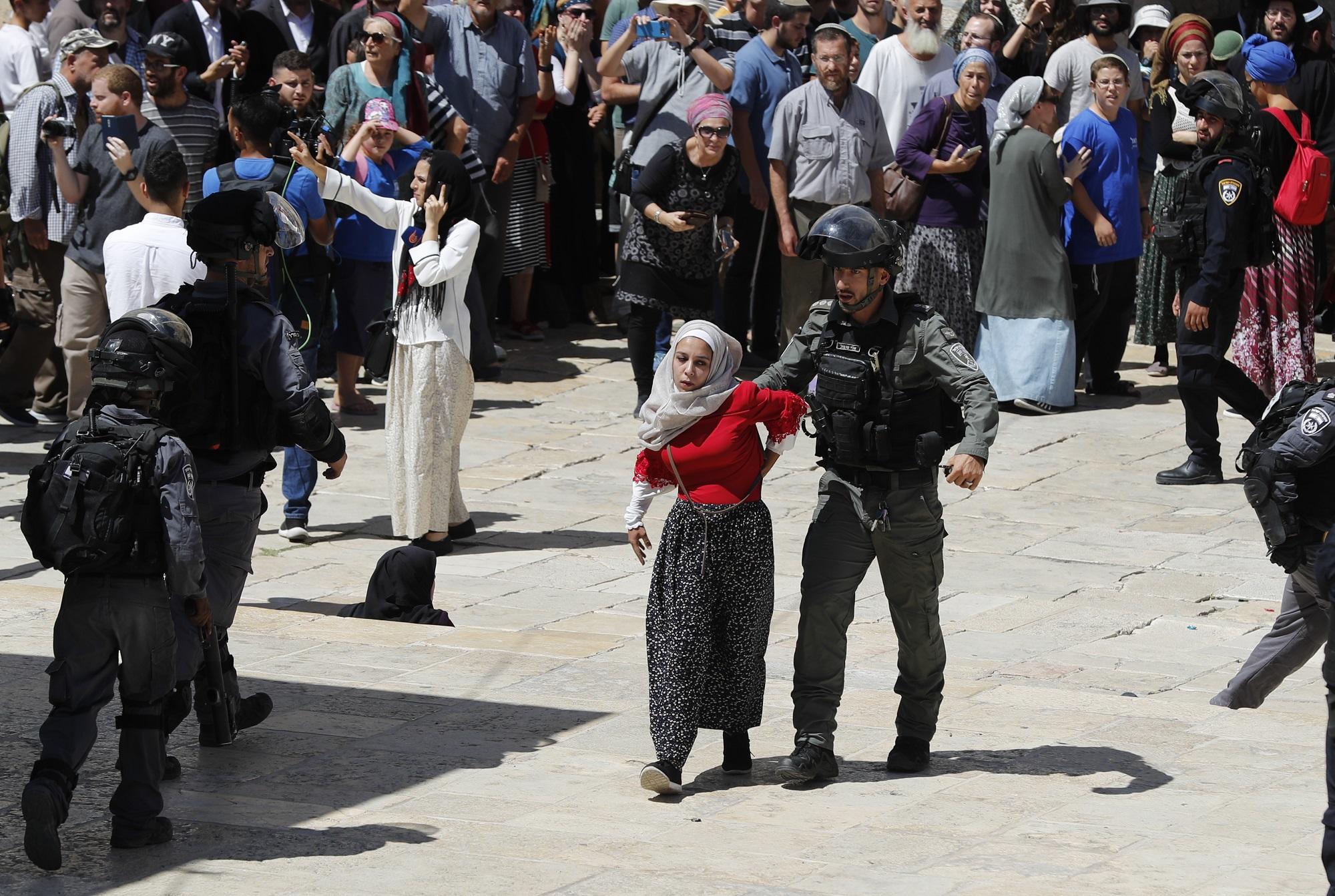 أحد عناصر قوات الاحتلال الإسرائيلي يعتقل فتاة فلسطينية بينما يقف خلفهما مستوطنون، خلال اقتحامات واسعة لباحات المسجد الأقصى، واعتداءات ضد المصلين، 11/08/2019. (أحمد غربلي/أ ف ب).