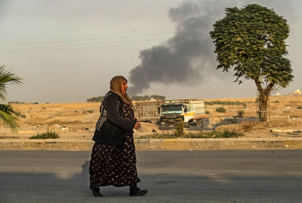 امرأة سورية تسير بمحاذاة دخان متصاعد إثر قصف تركي على بلدة رأس العين شمال شرق سوريا، 9 تشرين الأول/أكتوبر 2019. (دليل سليماني/ أ ف ب) 