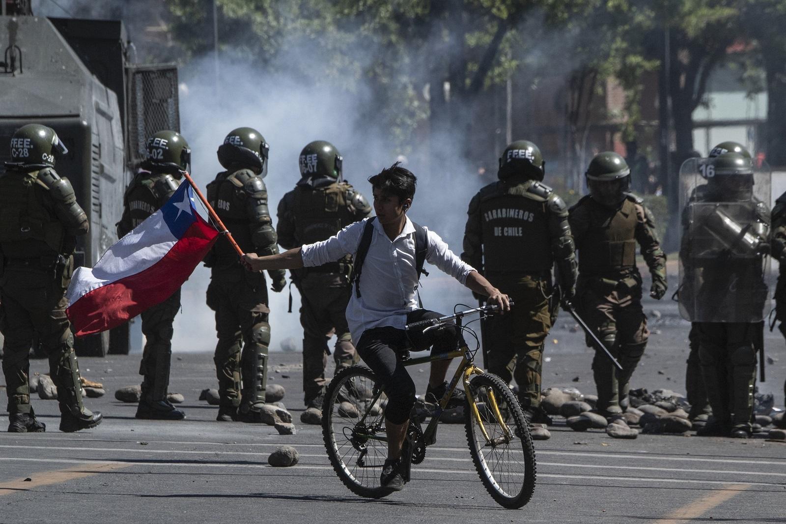 متظاهر على دراجة يلوح بعلم شيلي خلال اشتباك مع شرطة مكافحة الشغب في سانتياغو. 21 أكتوبر 2019. (أ ف ب)