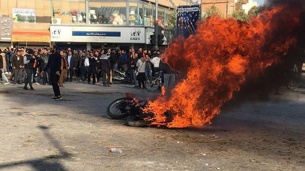 متظاهرون قرب دراجة نارية محترقة، في مدينة أصفهان وسط إيران، خلال احتجاجات ضد رفع أسعار البنزين. (أ ف ب)