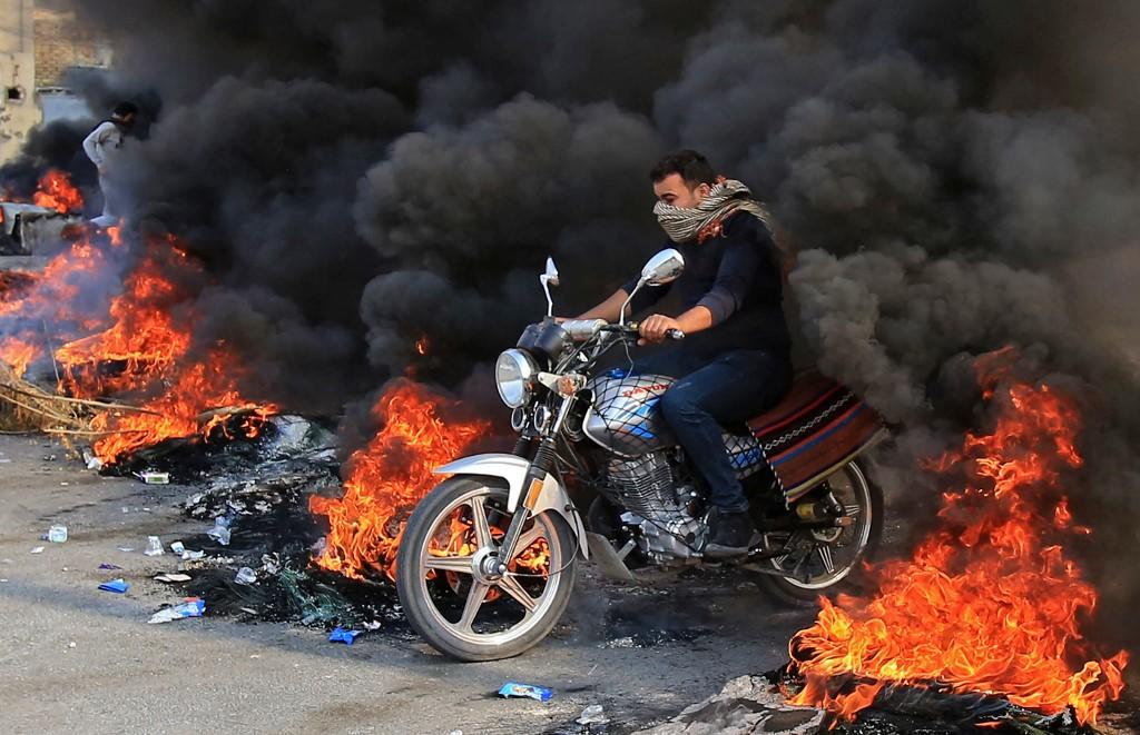 عراقي يقود دراجة نارية عبر إطارات محترقة في مدينة كربلاء جنوب العاصمة العراقية بغداد. 26/11/2019. محمد صواف / أ ف ب