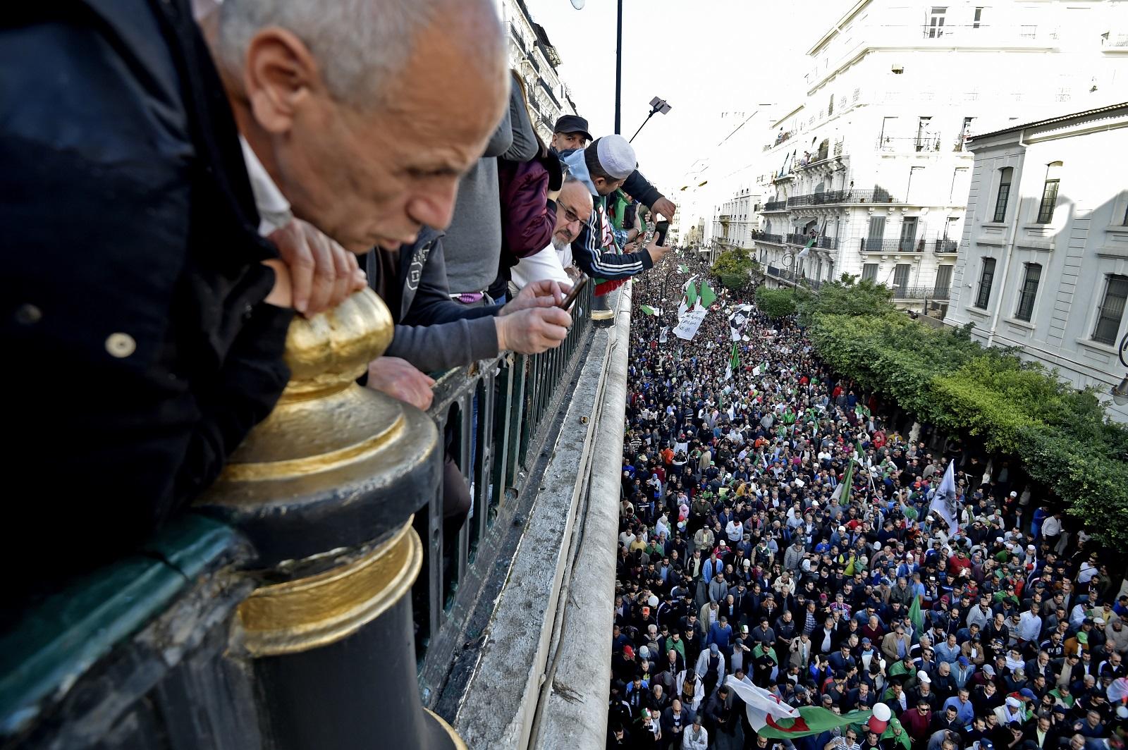 جزائريون يشاهدون متظاهرين مناهضين للحكومة يسيرون في العاصمة الجزائر. 6 ديسمبر 2019. (أ ف ب)
