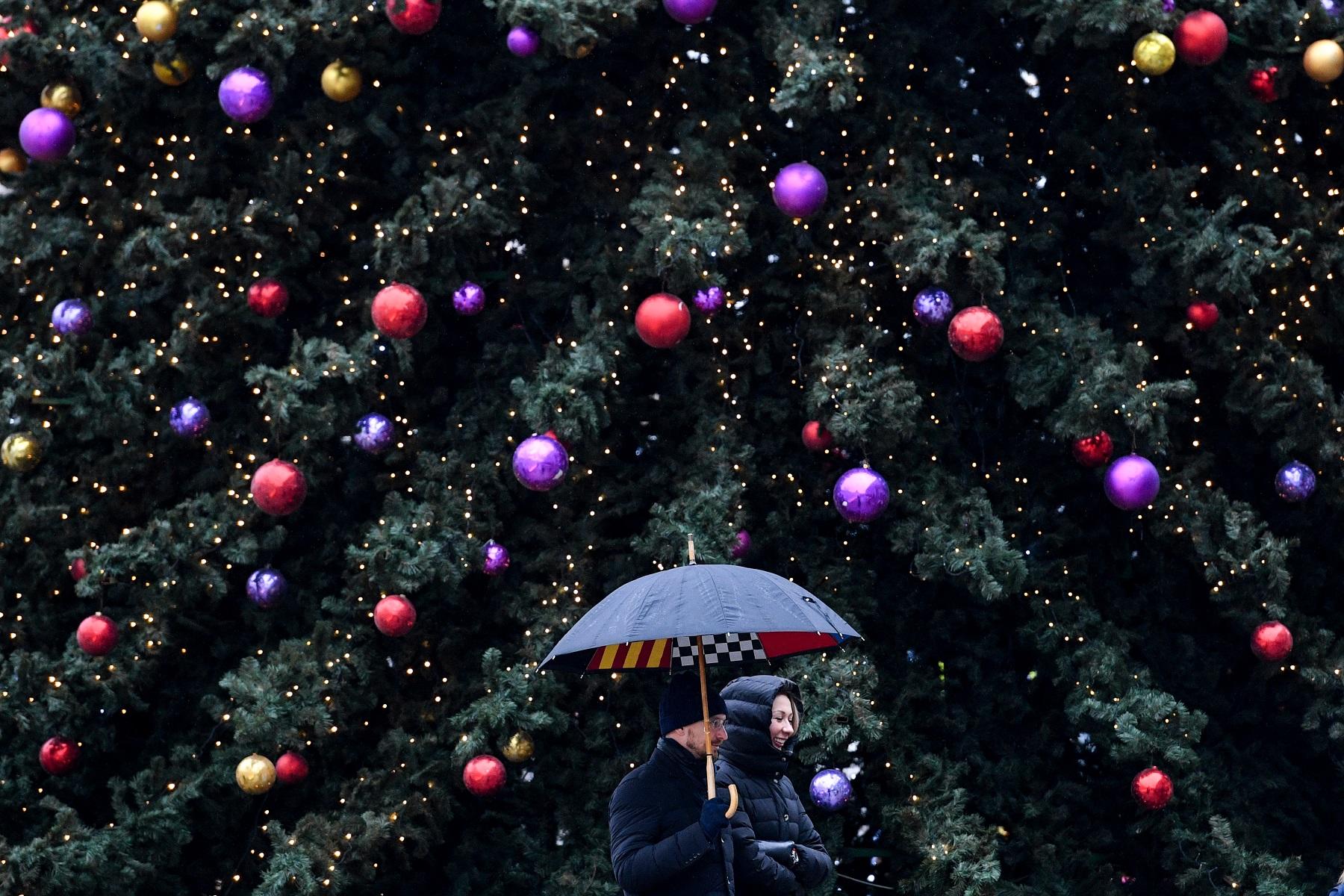 زوجان يمشيان أمام شجرة عيد الميلاد تحت المطر. 18 ديسمبر 2019. (أ ف ب)