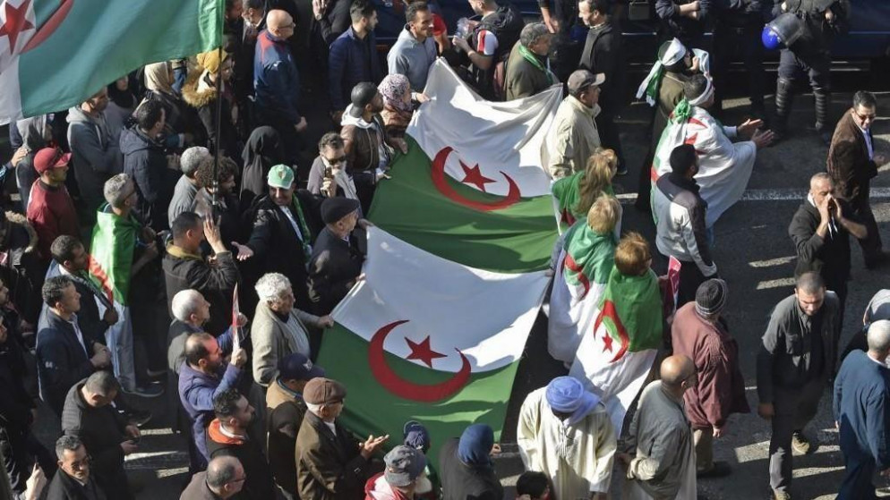 جزائريون يحملون أعلامًا وطنية كبيرة أثناء مسيرتهم في تظاهرة مناهضة للحكومة في العاصمة الجزائر. (أ ف ب)