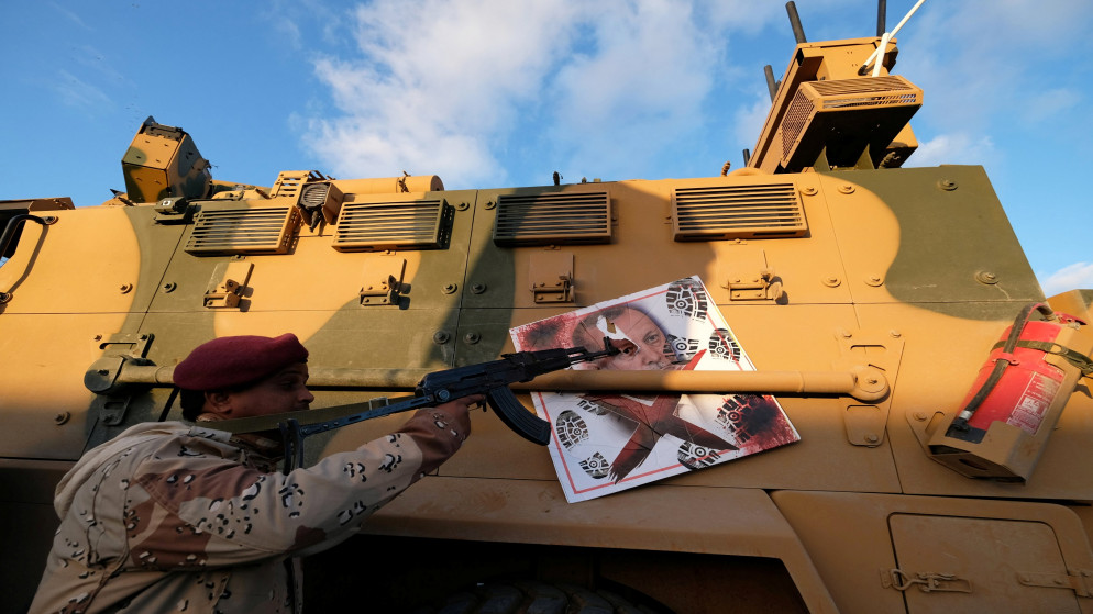 أحد أفراد قوات حفتر يشير ببندقيته إلى صورة الرئيس التركي رجب طيب أردوغان على مركبة مدرعة عسكرية تركية، 28 كانون الثاني/يناير 2020. (رويترز)