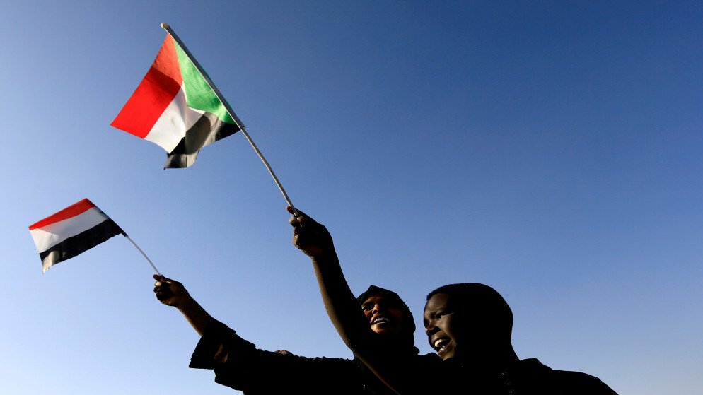 مواطنان سودانيان يرفعان علم بلادهما. (رويترز)