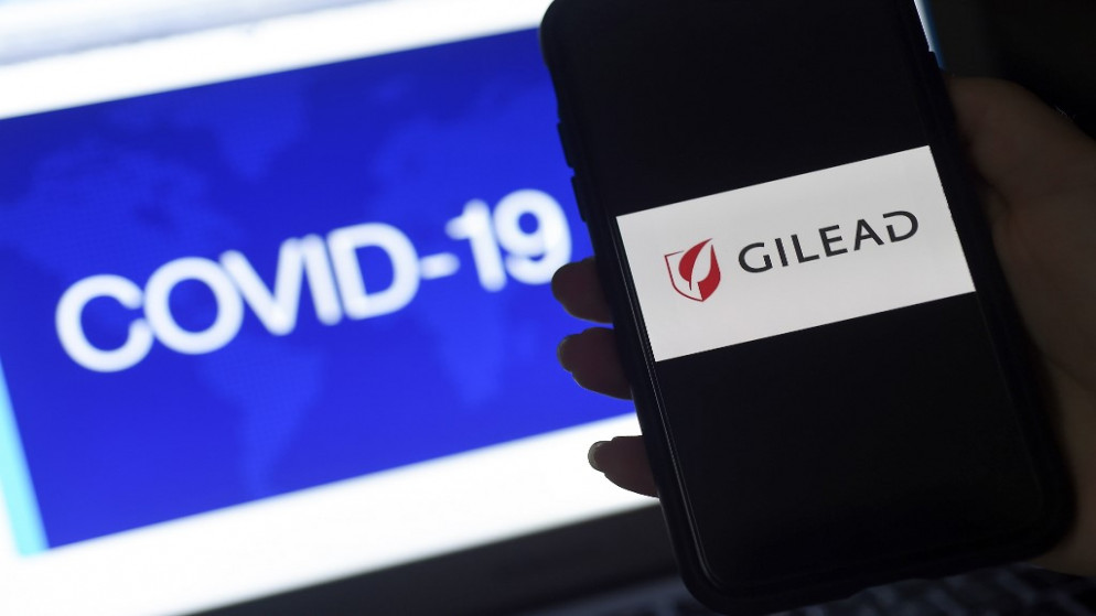 عرض شعار شركة "غلعاد" على هاتف ذكي بجوار شاشة تعرض رسم Covid-19 في أرلينغتون، فيرجينيا، 25 مارس 2020. (أ ف ب)