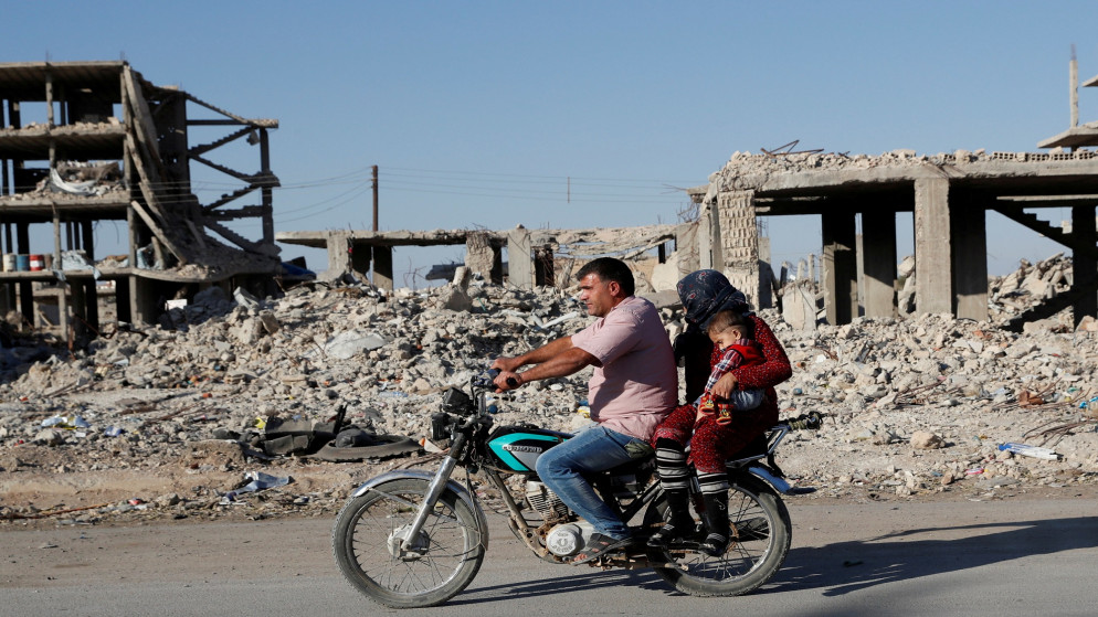 شخص يقود دراجة نارية مع عائلته أمام أنقاض مبانٍ دمرت خلال قتال في كوباني السورية. 11/10/2020. (إريك دي كاسترو / أ ف ب)