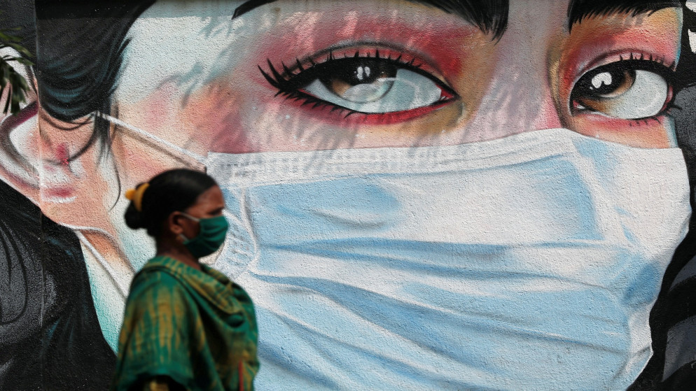 سيدة تمر أمام لوحة جدارية لفتاة ترتدي كمامات واقية وسط انتشار فيروس كورونا في مومباي الهندية. 23/10/2020. (فرانسيس ماسكارينهاس/ رويترز)