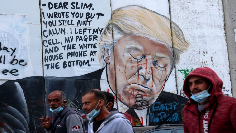 عمال فلسطينيون يعودون إلى منازلهم أمام لوحة جدارية تصور الرئيس الأميركي دونالد ترامب على طول مقطع من الجدار الفصل العنصري في مدينة بيت لحم. 03/11/2020. (إيمانويل دوناند / أ ف ب)