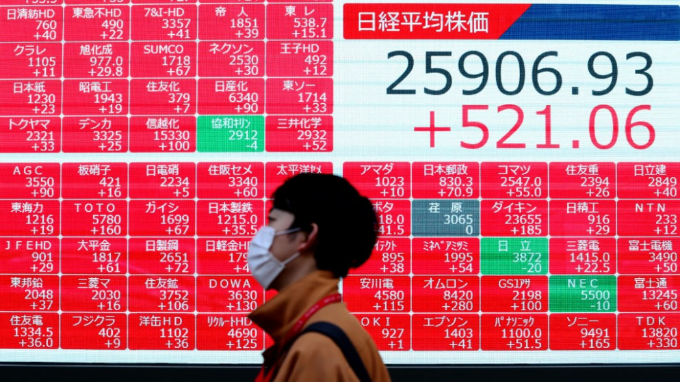 رجل يرتدي كمامة وجه للوقاية من كوفيد-19، يسير أمام لوحة إلكترونية تعرض أسعار الأسهم في بورصة طوكيو والأرقام الختامية لمؤشر نيكي في طوكيو. 16/11/2020. (أ ف ب)