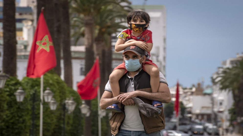 شخص يرتدي كمامة يحمل ابنه على كتفه أثناء سيرهم في وسط العاصمة المغربية الرباط. (أ ف ب)