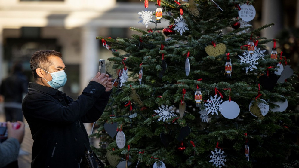 رجل يرتدي كمامة ويلتقط صورة لشجرة عيد الميلاد في كوفنت غاردن بوسط لندن،22 تشرين الثاني/نوفمبر 2020 (أ ف ب)