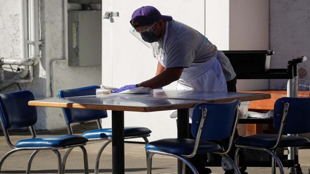شخص يمسح طاولة على رصيف خارج مطعم، ويرتدي معدات وقائية من فيروس كورونا في مقاطعة لوس أنجلوس، الولايات المتحدة، 30 تشرين الثاني/نوفمبر 2020. (رويترز)