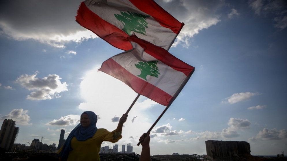 نساء لبنانيات يلوحن بالعلم الوطني خلال حفل لإحياء ذكرى ضحايا انفجار مرفأ بيروت مقابل ميناء العاصمة، في 11 آب/ أغسطس 2020. (أ ف ب)