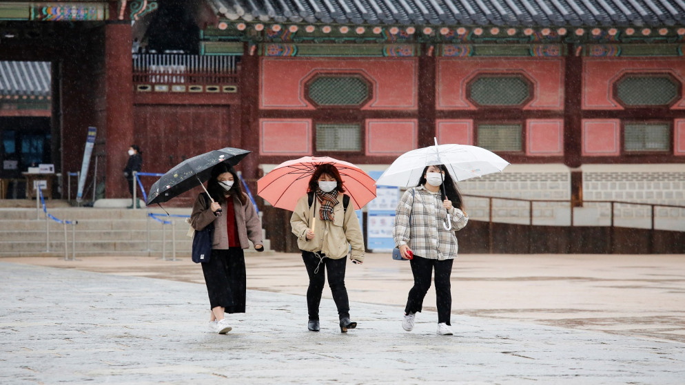 سائحون يرتدون الكمامات ويمشون مع المظلات أثناء هطول الأمطار في قصر كيونغ بوك في وسط سيول في كوريا الجنوبية (رويترز / هيو ران)
