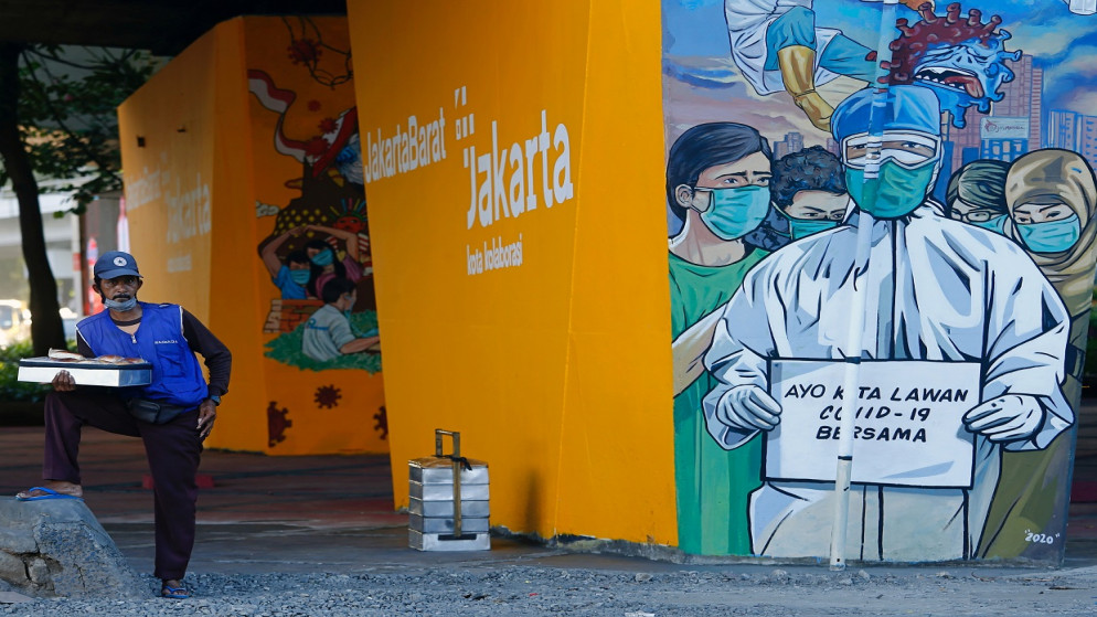 بائع يرتدي كمامة، ويقف بالقرب من لوحة جدارية تروج للتوعية من فيروس كورونا في إندونيسيا، 1 كانون الأول/ ديسمبر 2020.(رويترز / أجينج دينار أولفيانا)