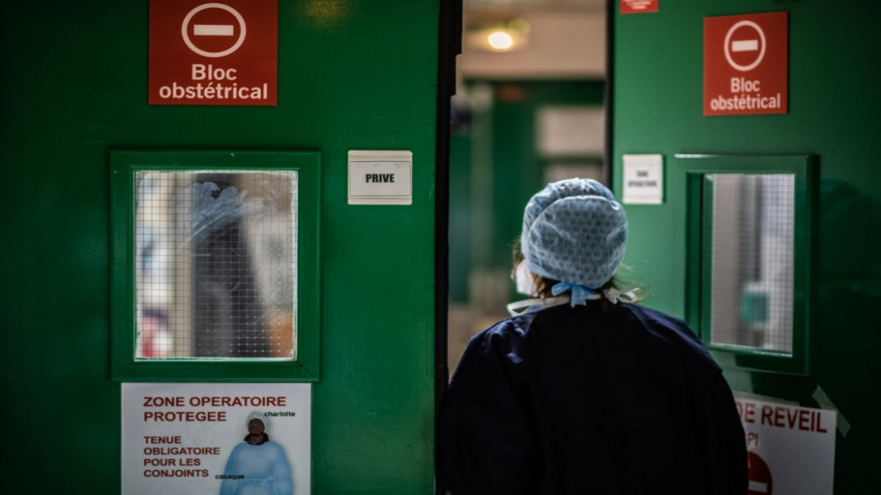 ممرضة في مستشفى دياكونيس الفرنسي، تمر من باب غرفة عمليات ولادة وترتدي معدات واقية في ظل أزمة جائحة كوفيد-19. 17/11/2020. (أ ف ب)