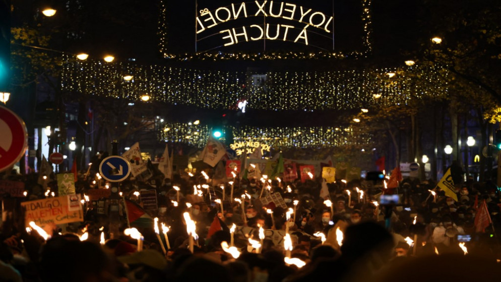 متظاهرون يرفعون الشموع خلال مظاهرة لتسوية أوضاع المهاجرين بمناسبة اليوم العالمي للمهاجرين في باريس، 18 كانون الأول/ديسمبر 2020 (أ ف ب)