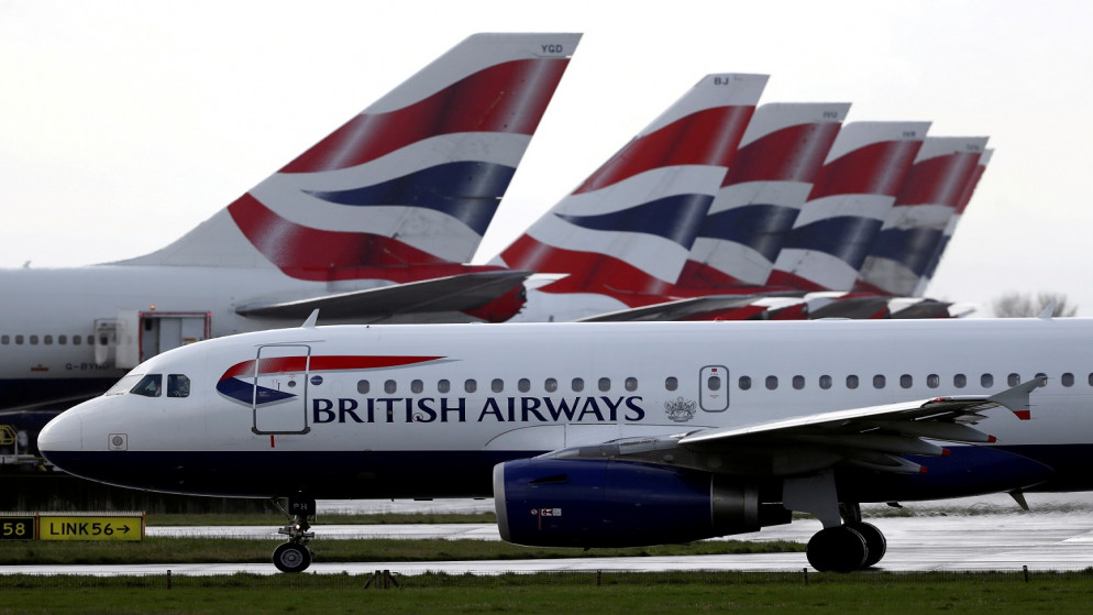 طائرة تابعة للخطوط الجوية البريطانية، تمر بزعانف ذيل طائرة متوقفة بالقرب من المبنى رقم 5 في مطار هيثرو بلندن، بريطانيا، 14 آذار/ مارس 2020. (أ ف ب)