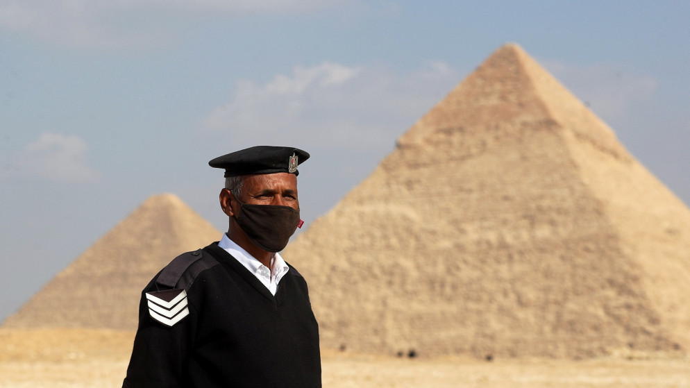 رجل أمن مصري يرتدي كمامة ويقف بالقرب من الأهرامات في الجيزة. (رويترز)