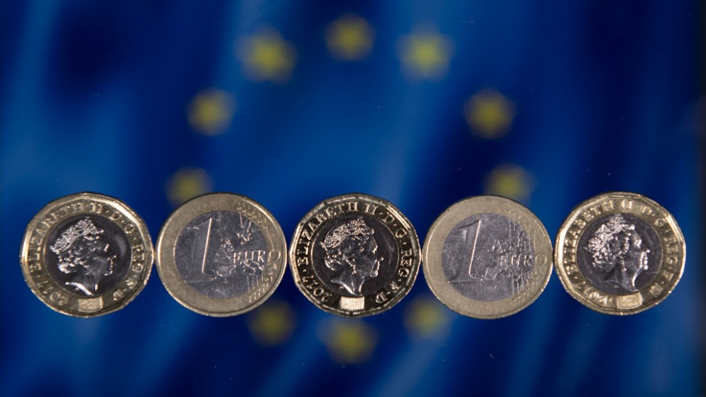 ترتيب عملات معدنية بريطانية بقيمة جنيه إسترليني واحد وعملات يورو واحدة أمام علم الاتحاد الأوروبي في صورة فوتوغرافية في لندن.(أ ف ب)