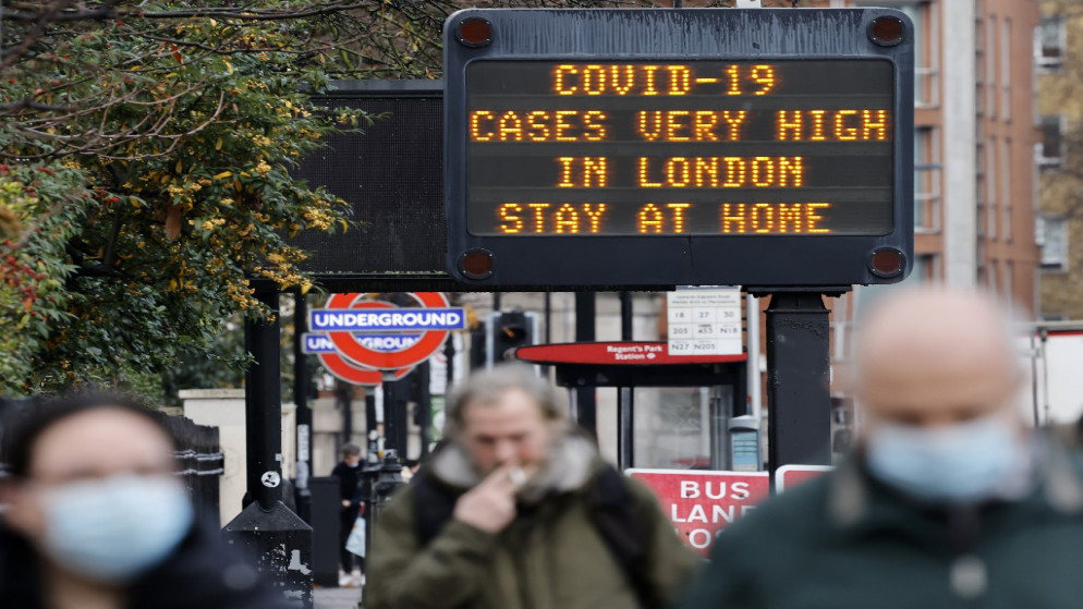 أشخاص يرتدي بعضهم كمامات للوجه؛ بسبب جائحة COVID-19، أمام لافتة تنبه الناس إلى أن "حالات الإصابة بكوفيد -19 مرتفعة للغاية في لندن - ابق في المنزل"، لندن، 23 كانون الأول/ ديسمبر 2020. (أ ف ب)