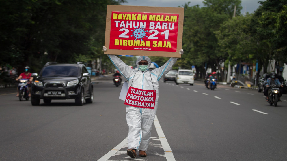 رجل يرتدي ملابس واقية ويحمل لافتة كتب عليها احتفال بليلة رأس السنة 2021 في المنزل؟ و؟ الالتزام بالبروتوكولات الصحية؟ في إندونيسيا. 31/12/2020. (رويترز)