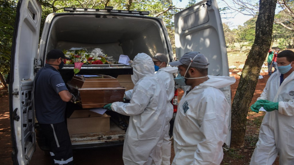 موظفون ينقلون جثثا لأشخاص كانوا مصابين بفيروس كورونا في البرازيل. (أ ف ب)