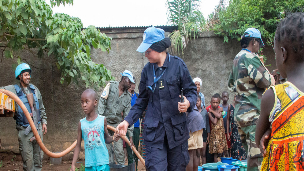 نادية خليفي، هي ظابطة حفظ سلام تونسية تعمل مع بعثة الأمم المتحدة لتحقيق الاستقرار في جمهورية أفريقيا الوسطى، تساعد صبيا على حمل دلو ماء إلى منزله. (الأمم المتحدة)