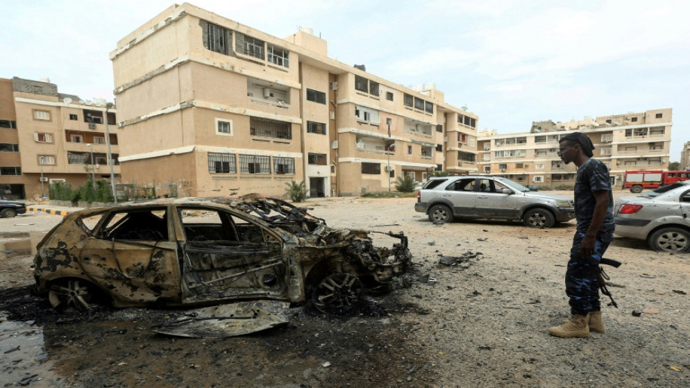 مقاتل موالٍ لحكومة الوفاق الوطني في ليبيا، يقف أمام هيكل سيارة مدمرة نتيجة قصف، في طرابلس، 9 أيار/مايو 2020. (أ ف ب)