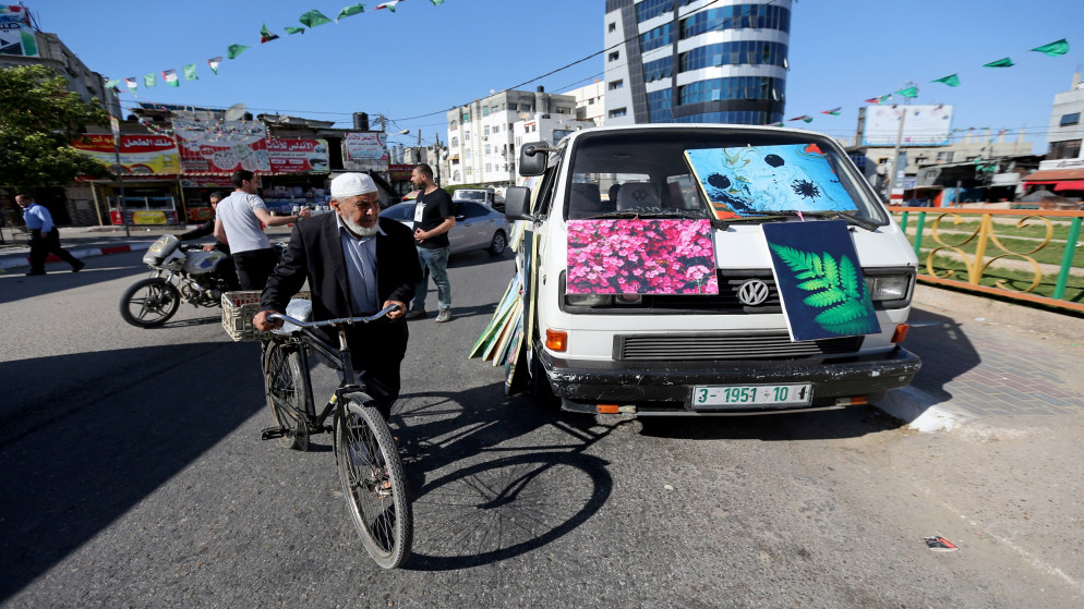 رجل يقود دراجته أمام حافلة صغيرة تعرض لوحات فنية للبيع في قطاع غزة وسط انتشار فيروس كورونا. 03/05/2020. (إبراهيم أبو مصطفى/ رويترز)