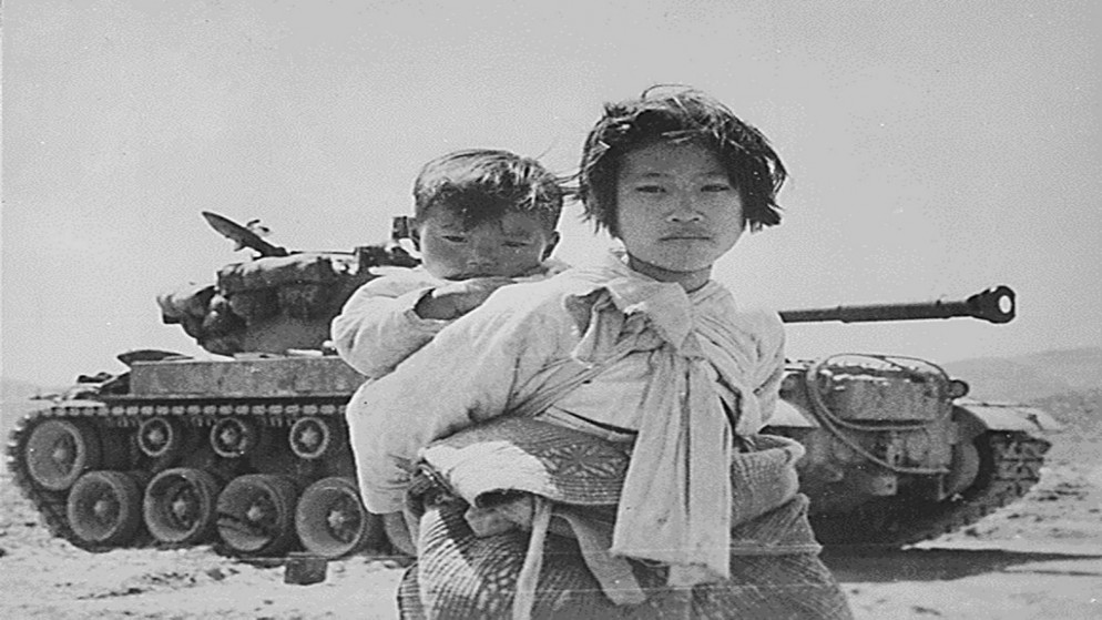 فتاة تحمل شقيقها أمام دبابة (M-26) قرب مدينة غويانغ في كوريا الجنوبية، 9 حزيران/يونيو 1951. (أ ف ب)
