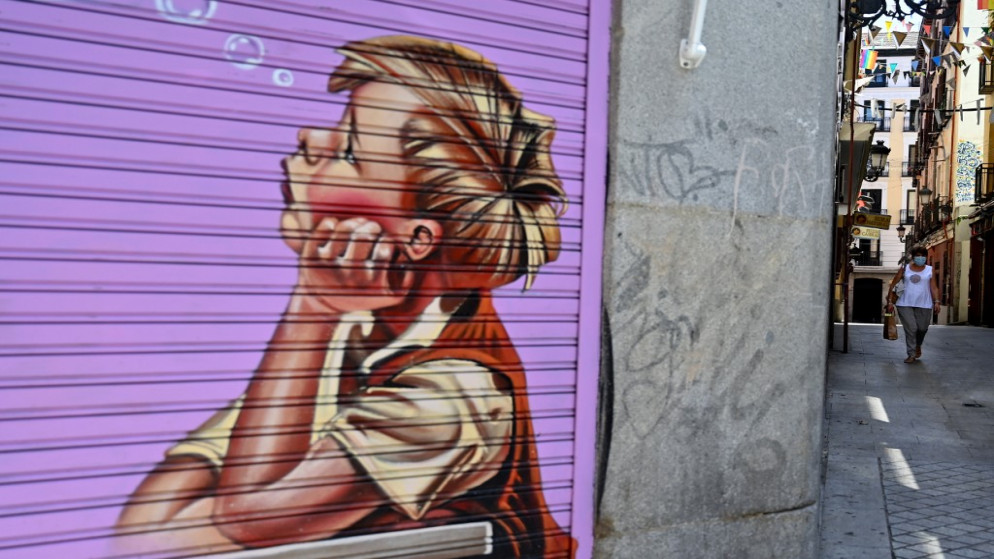 امرأة تسير في شارع في العاصمة الإسبانية مدريد بين متاجر مغلقة ضمن إجراءات احترازية للحد من انتشار فيروس كورونا المستجد في البلاد، 9 تموز/يوليو 2020. (أ ف ب)