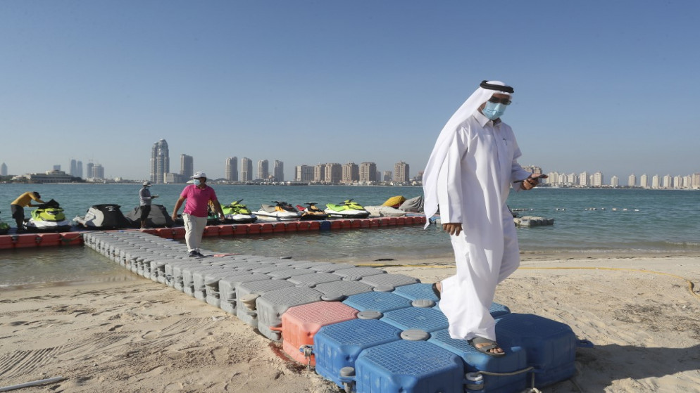 رجال يرتدون كمامات واقية ، يسيرون على رصيف بلاستيكي على شاطئ في العاصمة القطرية الدوحة.1 يوليو 2020.(أ ف ب)