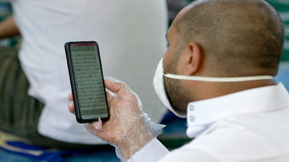 مصلّ يتلو القرآن الكريم عبر هاتفه في أحد مساجد عمّان. (أ ف ب)