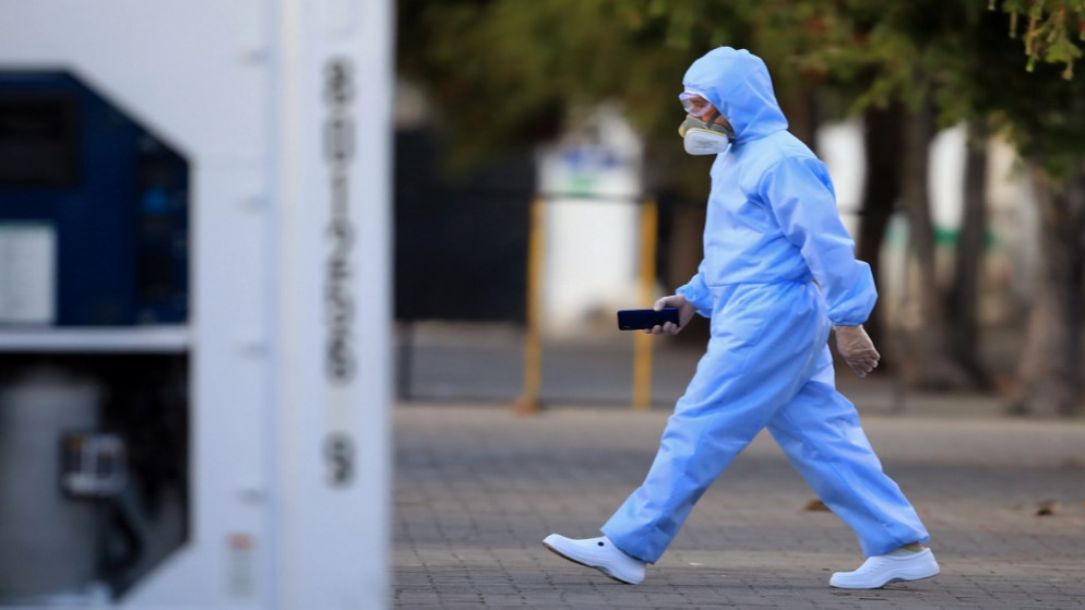 شخص يرتدي غطاء وقائيًا كإجراء وقائي ضد انتشار الفيروس التاجي الجديد COVID-19 ، يمشي بالقرب من حاوية مبردة في مقبرة في بوغوتا، 31 يوليو 2020. (أ ف ب)
