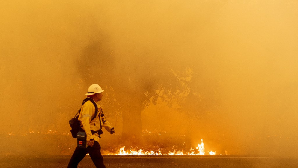 رجل إطفاء يعمل بالغاز والكهرباء في المحيط الهادئ يسير على طريق مع اقتراب ألسنة اللهب في فيرفيلد، كاليفورنيا خلال حريق مجمع لايتنينغ، 19 أغسطس 2020. (أ ف ب)