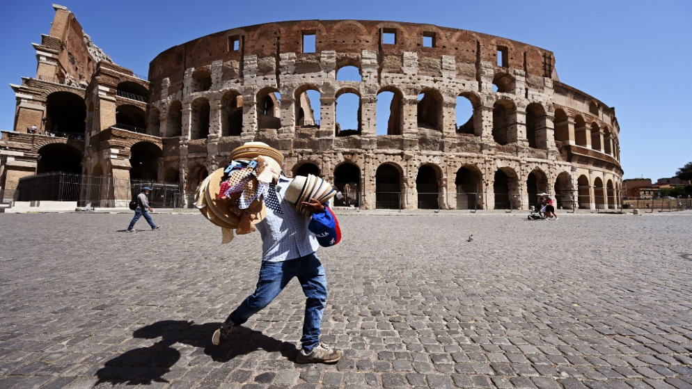 بائع متجول يحمل قبعات من القش أمام المدرج الروماني الكولوسيوم في العاصمة الإيطالية روما، 22 آب/أغسطس 2020. (فيتشينزو بينتو/ أ ف ب)