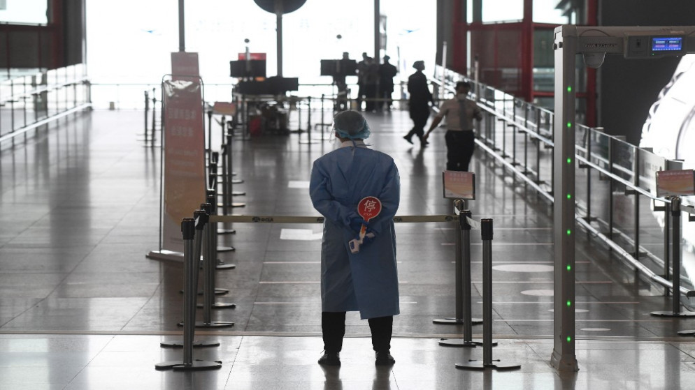 عاملة ترتدي ملابس واقية تنتظر للتحقق من درجة حرارة الركاب الذين يدخلون المطار في بكين. 18/06/2020. (أ ف ب)