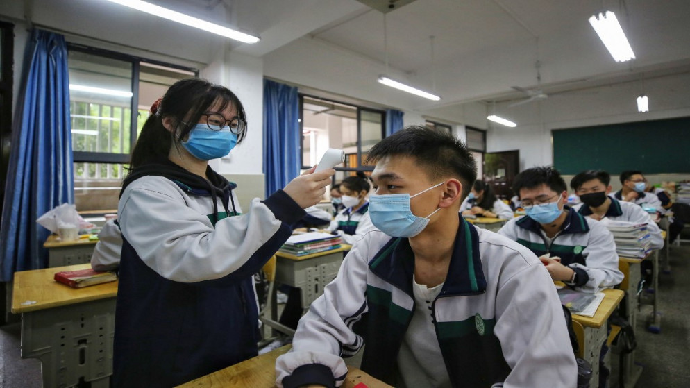 طالبة في مدرسة ثانوية تتحقق من درجة حرارة جسم زملائها، في ووهان مقاطعة هوبي وسط الصين، 6 مايو 2020. (أ ف ب)