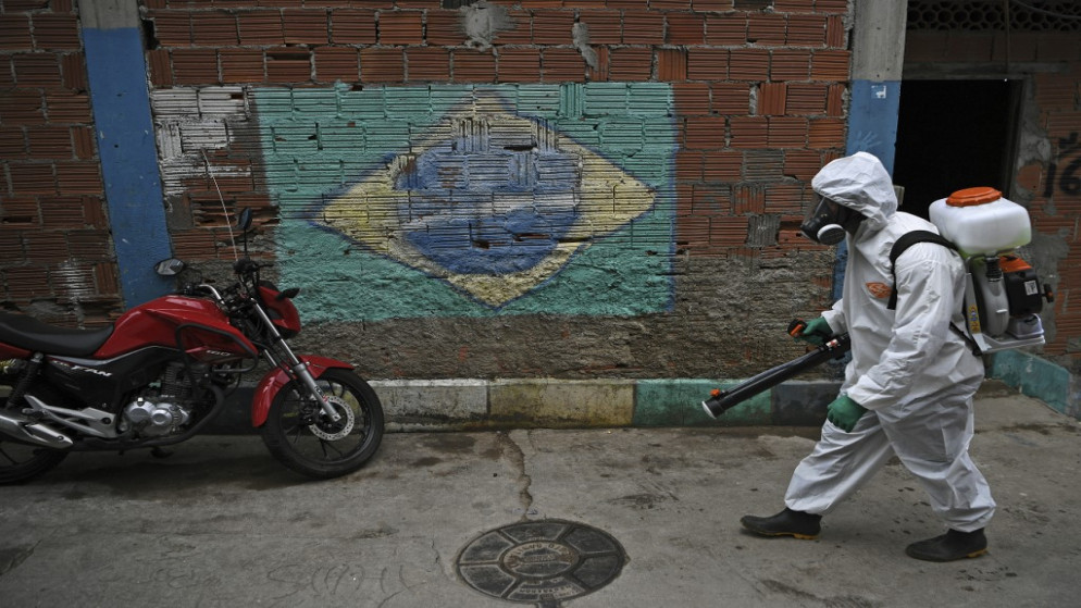متطوع يرتدي معدات الوقاية الشخصية أمام لوحة جدارية تصور العلم البرازيلي، أثناء تطهير منطقة في بابلونيا فافيلا، البرازيل. 18 أبريل 2020. (أ ف ب)